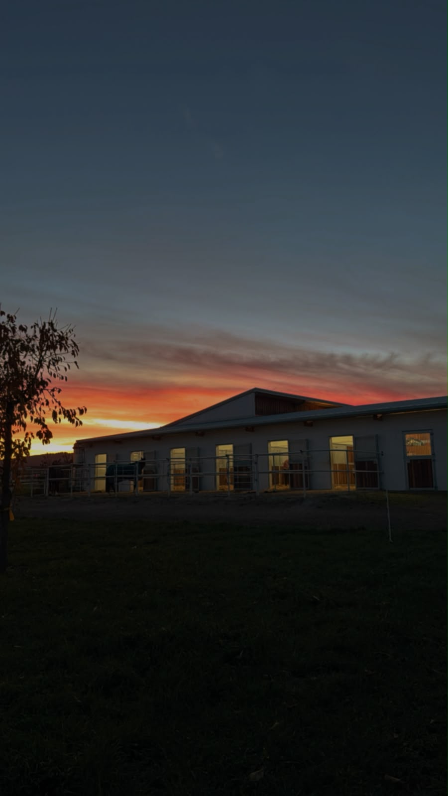 Stallgebäude mit Boxen und Paddocks im Sonnenuntergang